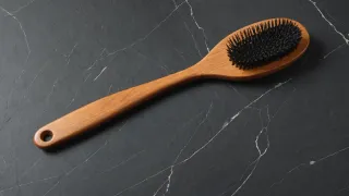 Brosse à cheveux en bois à poils noirs posée en diagonale sur un plan de travail en ardoise sombre veinée de blanc, lumière du jour diffuse